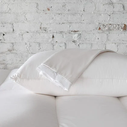St. Genève Absolute Pillow Protector on a bed with white pillows against a white brick wall