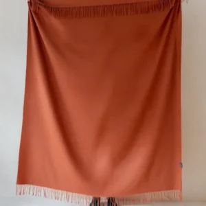 TBCo Lambswool Blanket in Rust Melange with fringed edges displayed against white wall, showcasing luxurious wool texture