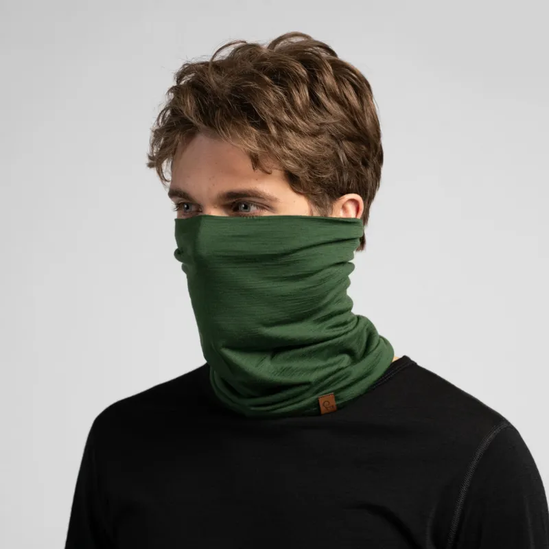 A studio portrait of a man looking off to the left. He is wearing a black long-sleeved shirt and a dark green neck gaiter pulled up to cover his lower face and nose.