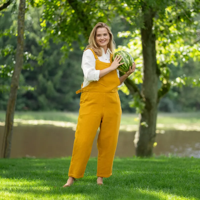 Woman in yellow Nicci linen jumpsuit holding a watermelon slice in a park like setting
