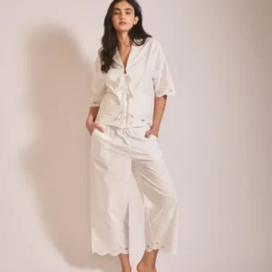 Woman wearing TBCo Cropped Cotton Pyjamas in White Shell with scalloped eyelet hem and relaxed cropped trousers standing against plain backdrop