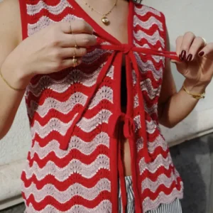 Close-up of a woman adjusting TBCo Cotton Knitted Vest in Pink Wave with red and pink wavy knitted pattern outdoors
